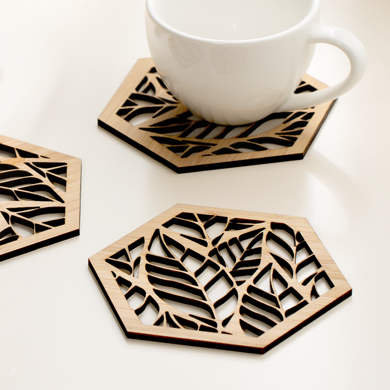 Posavasos hexagonales calados en tablero de bambu, con un motivo de hojas, junto a una taza de cafe