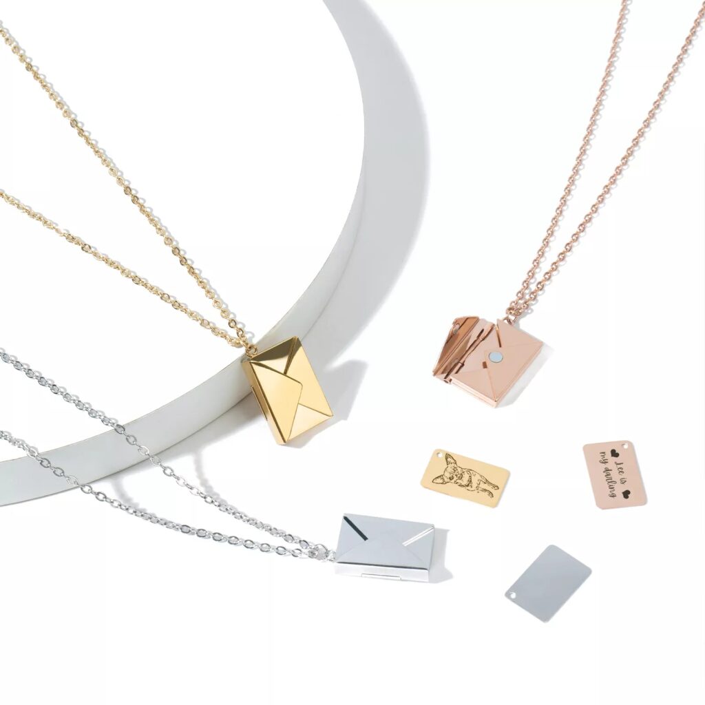 Los tres collares de sobre en oro, oro rosa y plata, con sus cadenas y las tarjetitas grabables fuera del colgante, una con un perro y otra con un texto