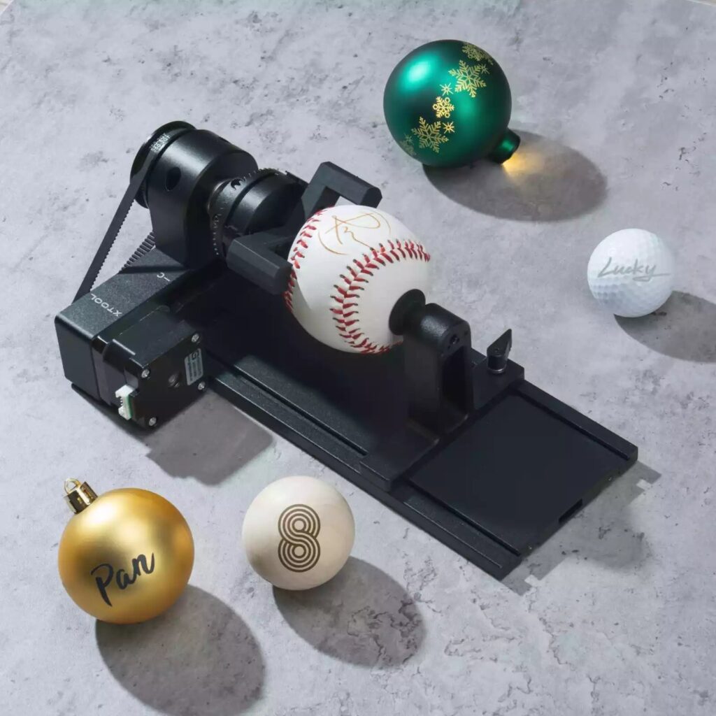 Rotativo xTool RA2 Pro grabando una pelota de beisbol, junto a bolas de navidad y una pelota de golf grabadas